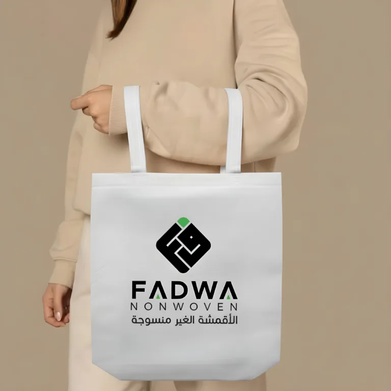 A close-up view of a person wearing a beige long-sleeved outfit holding a premium white non-woven box shopping bag with thick, durable white fabric strap handles.