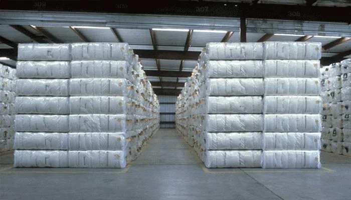 An interior perspective of a large industrial warehouse filled with symmetrical rows of stacked pallets holding packed, white non-woven bags ready for distribution and logistics.