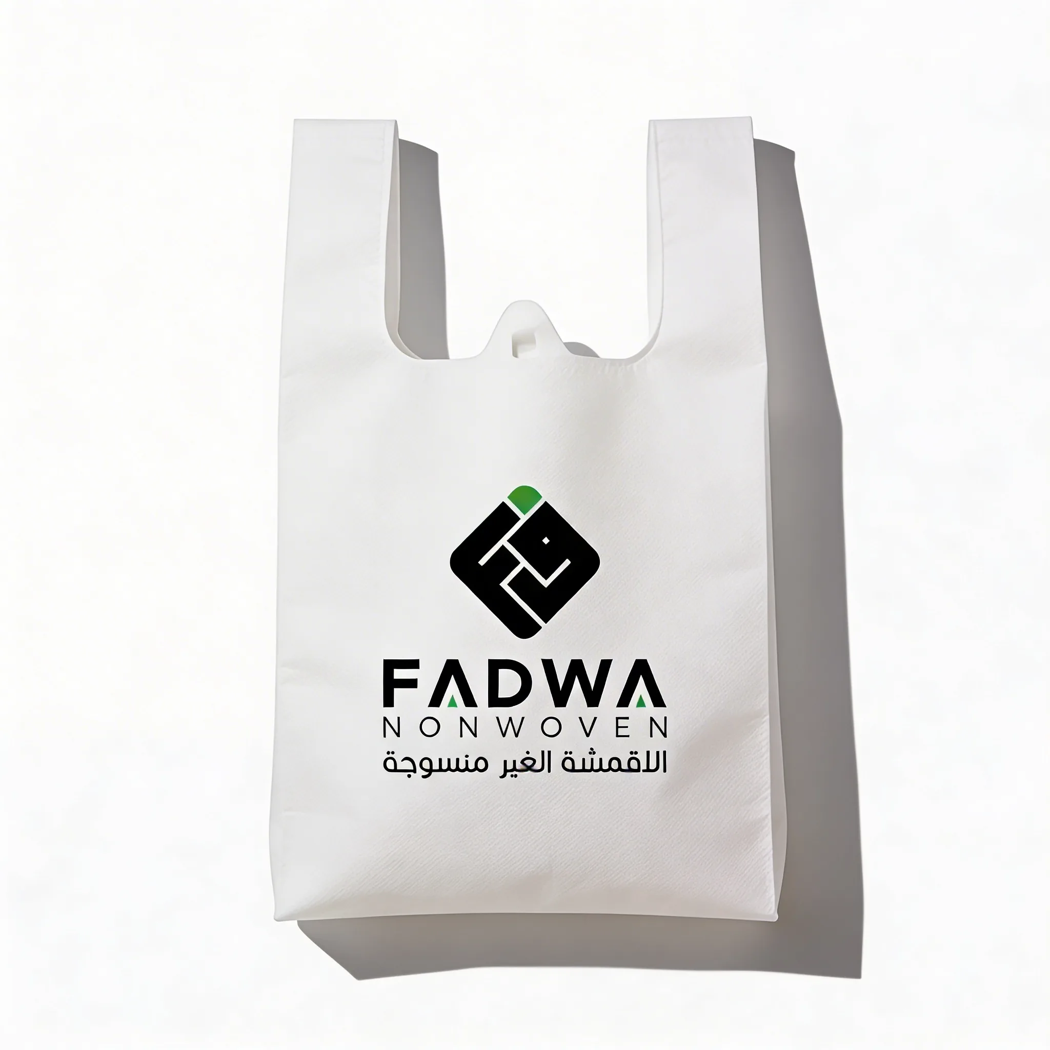 A plain white non-woven T-shirt bag with vest handles, featuring a high-quality print of the black and green Fadwa corporate logo centered on its front surface.