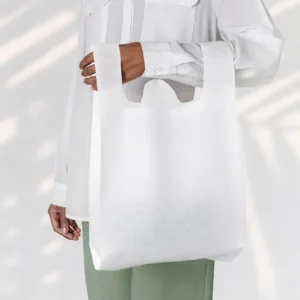 A close-up photograph showcasing a white non-woven T-shirt shopping bag draped over a person's arm wearing a white long-sleeved dress shirt, highlighting the texture and handle loops of the fabric.