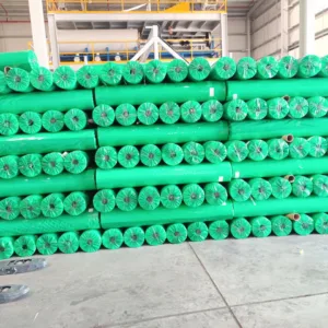 A large warehouse stack of green-wrapped rolls of non-woven PP agricultural crop cover fabric ready for shipment.