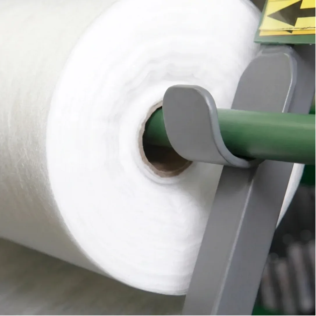 Close-up of an industrial non-woven fabric roll making machine winding a large roll of white non-woven material during the manufacturing process.